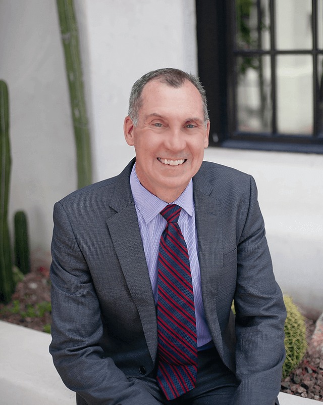 A merit systems protection board expert, Robert P. Erbe, sitting in front of a garden containing cactuses in Tucson.